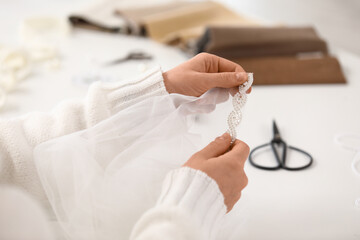 Female tailor's hands sewing wedding dress at table in atelier, closeup