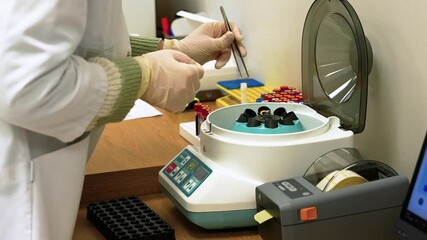 A close-up shot of a lab technician carefully handling blood samples using a centrifuge in a well-equipped laboratory. Bright lighting highlights the precise actions and modern equipment.