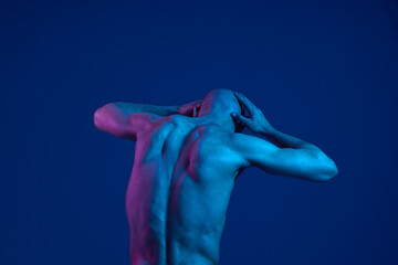 Obraz premium A man poses dramatically against a blue background, showcasing his muscular physique with vibrant lighting. The image emphasizes emotion and artistic expression, creating a striking visual impact.