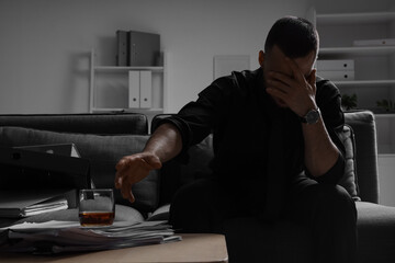 Businessman taking drink from table in dark office. International Stress Awareness Week
