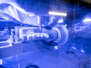 High-precision CNC milling machine processing zirconia dental restoration under bright blue LED light in laboratory.