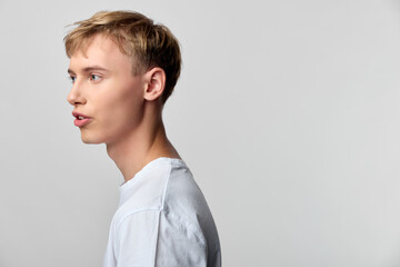 Profile of a young man in a white shirt speaking to the left, studio lighting and a clean neutral...
