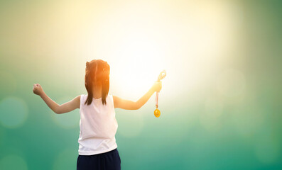 A girl holding a gold medal against a sunset sky background