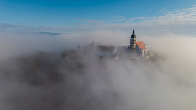 Eine Kirche steht in der Nebellandschaft auf einem H&uuml;gel am Morgen in Deutschland