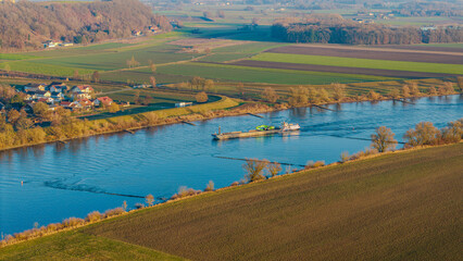 Blick auf einen Fluss mit einem Schiff, Wiesen und Felder im Hintergrund