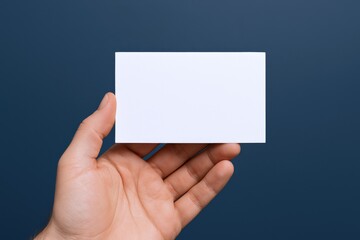 Fototapeta premium Hand Holding Blank White Business Card Mockup Against Dark Blue Background for Product Placement