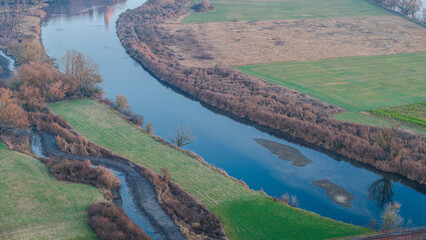Ein Fluss schl&auml;ngelt sich durch die Landschaft mit Wiesen und B&auml;umen, aufgenommen in der D&auml;mmerung