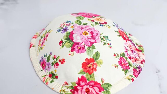 Floral patterned cushion on white background. Features pink, red flowers, green leaves on white canvas, pleated edge