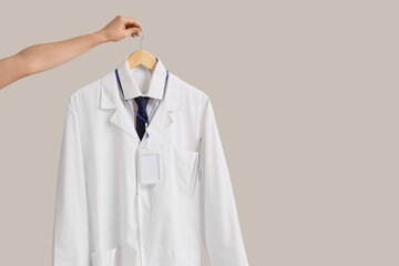 Female hand with hanging doctor's uniform on light background