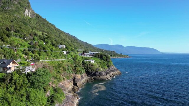 Puerto Montt, Chile: Aerial view of coastal road along pacific ocean in Puerto Montt, Lake District heading to carratera austral road, Chile with backward motion showing wooden houses by the cliff