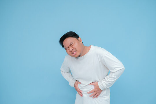 a young asian man has stomach ache hand expression when having stomach ache with strange face 