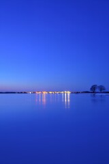 Serene lake at dusk with city lights reflecting on calm water