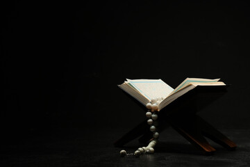 Wooden stand with Koran and prayer beads for Ramadan on black background