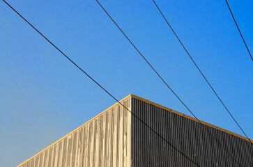 Detail of contemporary building corner with vertical wooden slat siding against a blue sky, bisected by parallel black power lines stretching diagonally across the frame.