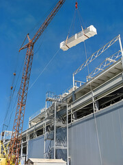 Construction crane lifting large building module onto industrial structure against blue sky