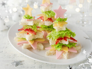 Festive Christmas fir tree canape with cheese, salami, mortadella and bread against  light backdrop of festive served family dinner on background of bokeh lights.