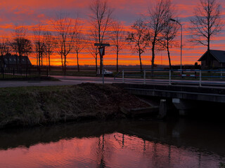 A sunset in a little village in the Netherlands with a channel in the foreground with reflection of the sky
