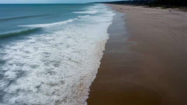 Serene Aerial View of Waves Crashing on Sandy Beach with People Walking