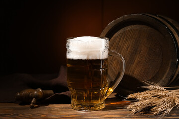 Wooden barrel and mug of cold beer on table against dark background