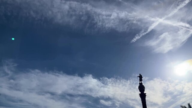 Statue of Christopher Columbus standing atop the Columbus Monument, reaching towards the sea under a vibrant blue sky with wispy clouds, symbolizing exploration, travel, and historical landmarks