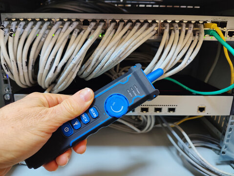 Technician Using a Digital Network Cable Tracker Probe to Identify and Test Ethernet Connections in a Server Rack Patch Panel