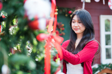 A young woman is decorating a Christmas tree with ornaments, getting ready for the winter holiday season. It's a celebratory scene in front of the house.
