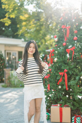 A young woman is decorating a Christmas tree with ornaments, getting ready for the winter holiday season. It's a celebratory scene in front of the house.