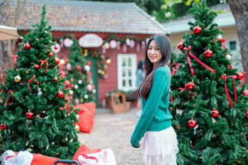 A young woman is decorating a Christmas tree with ornaments, getting ready for the winter holiday season. It's a celebratory scene in front of the house.