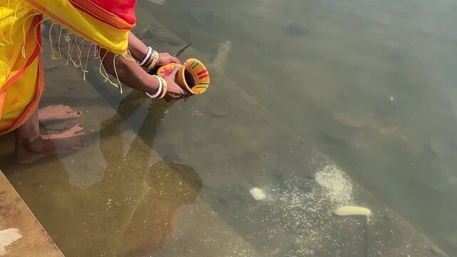 An Indian bride in yellow saree picking water from the River Ganga in a pot for wedding in India 