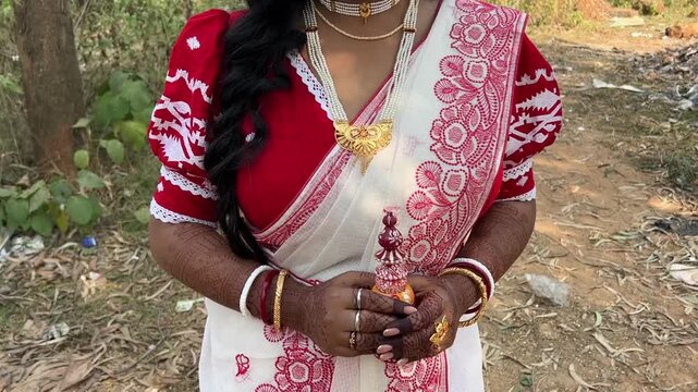 A Bengali bride in red and white saree standing outdoor holding a sindur box for wedding in India