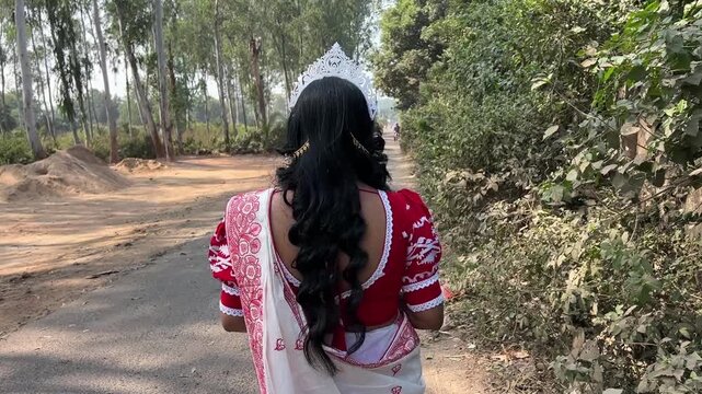 Rear shot of a Bengali bride in red and white saree walking in a forest in India