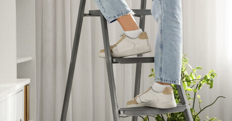 Legs of woman standing  on stepladder in room