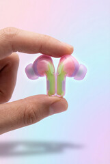 Hand Holding Translucent Pink and Green Wireless Earbuds Against Gradient Background