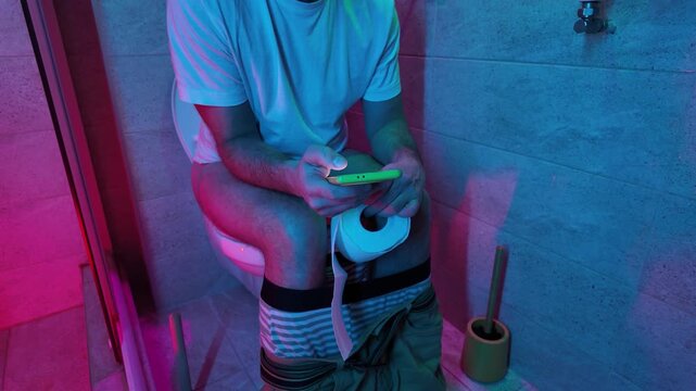 Man using smartphone while sitting in a toilet.