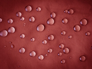 Red waterproof fabric with large raindrops close-up