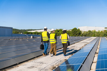 Three engineers walking among rows of solar panels on a commercial building roof, working on sustainable energy and green power © Koldo_Studio