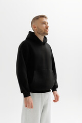 Man wearing black hoodie stands against white background with neutral expression during indoor shooting session