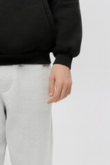Hand of a person wearing a black sweater and gray sweatpants, showing style in casual fashion