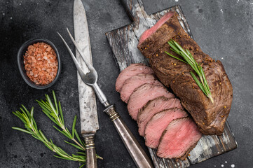 Juicy roast beef sliced medium rare on rustic wooden board with herbs and seasoning on dark background with copy space