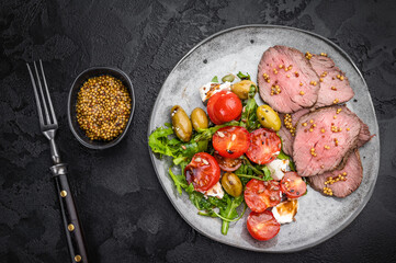 Roast beef salad with medium rare beef slices arugula tomatoes olives and cheese on dark stone background top view copy space