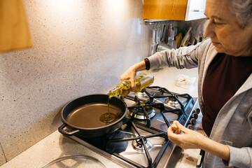 Woman pouring olive oil from a bottle into a frying pan on a gas stovetop