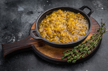 Homemade cucumber relish condiment in cast iron pan on rustic wooden board dark stone background overhead view