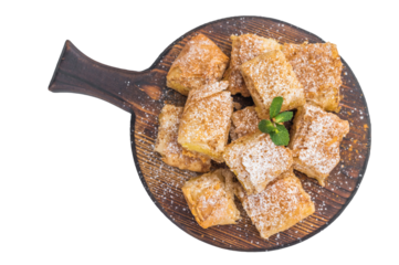 Greek custard pie bougatsa made with flaky filo pastry cut into squares served on round wooden board with powdered sugar