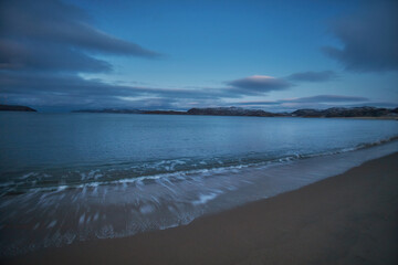 Fototapeta premium View of the coast in Teriberka, Russia, during twilight with calm water and distant hills visible on the horizon