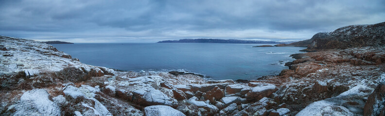 View of Teriberka coast in Russia during winter with snow covered landscape and calm sea under cloudy sky