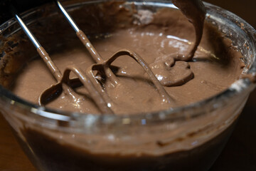 Mixing chocolate cake batter with the help of electric blender in a glass bowl
