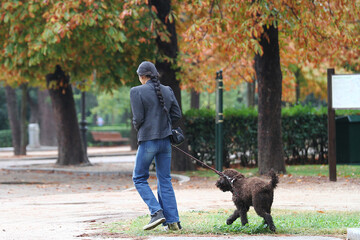Mujer paseando a perro de agua con correa de paseo por el parque y naturaleza en oto&ntilde;o