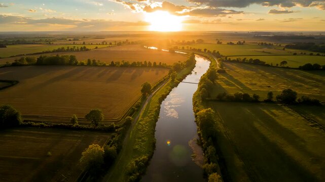 Aerial view of winding river flowing through agricultural fields at golden sunset light