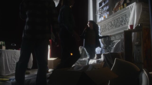 Handheld following shot of young people entering abandoned house holding flashlights and settling down in secret hideout, focus flowing from legs to full length view scene