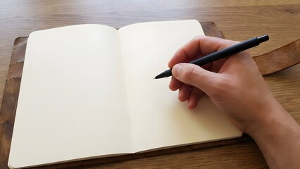 Hand holding pen over open notebook on wooden desk.